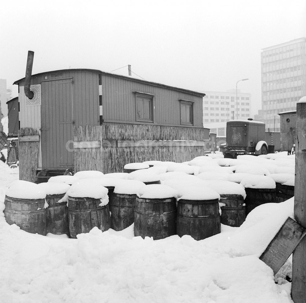DDR-Fotoarchiv: Berlin - Bauwagen mit Ofenrohr und schneebedeckte Fässer auf einer Baustelle in Berlin, der ehemaligen Hauptstadt der DDR, Deutsche Demokratische Republik