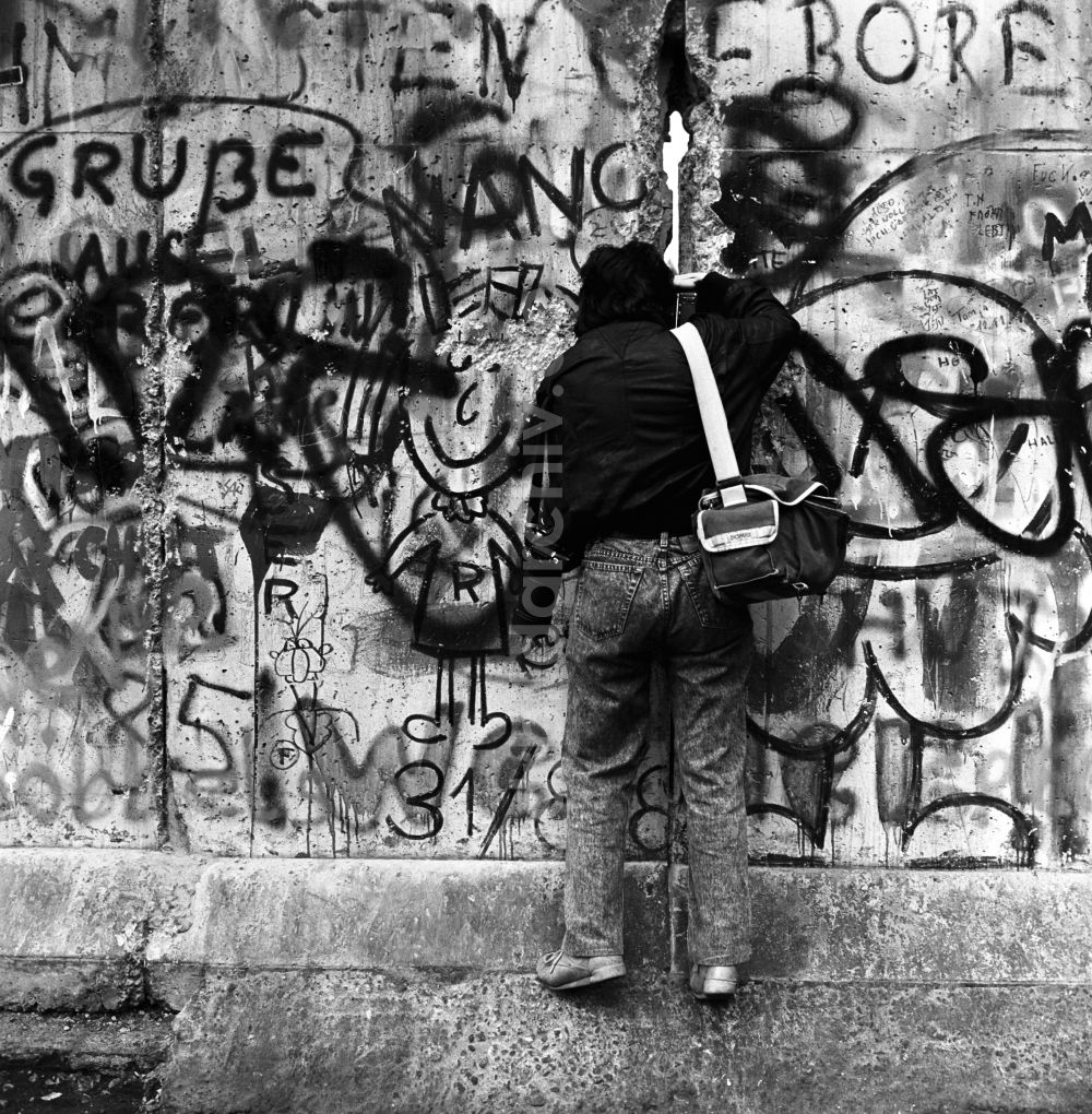 Berlin - Mitte: Ein Fotograf fotografiert durch einen Spalt in der Berliner Mauer in Berlin