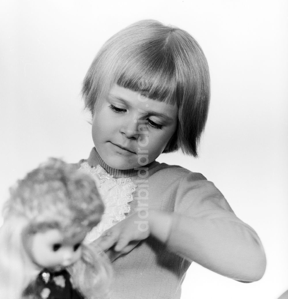 DDR-Fotoarchiv: Berlin - Ein kleines Kind spielt mit einer Puppe in Berlin, der ehemaligen Hauptstadt der DDR, Deutsche Demokratische Republik