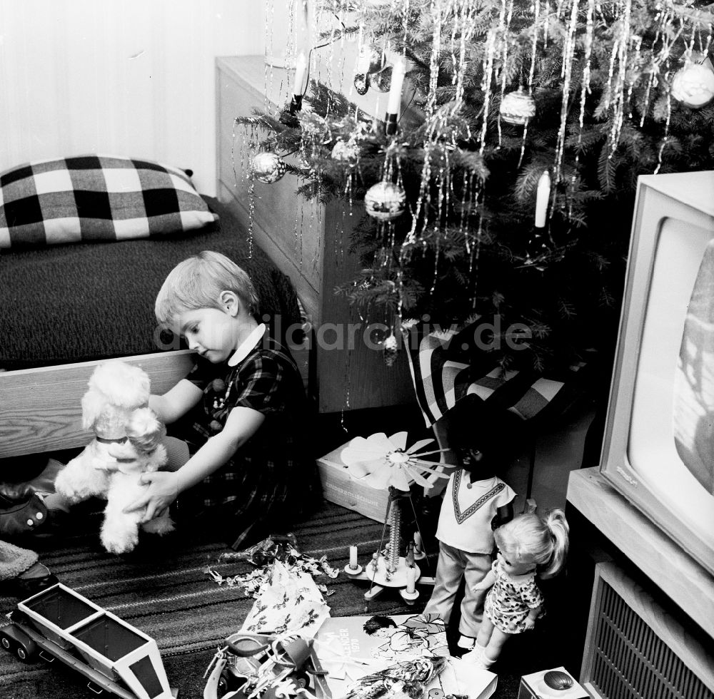 DDR-Fotoarchiv: Berlin - Ein kleines Kind spielt mit seinen Weihnachtsgeschenken unterm Weihnachtsbaum in Berlin, der ehemaligen Hauptstadt der DDR, Deutsche Demokratische Republik