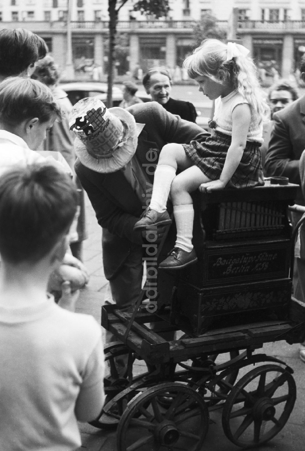 DDR-Fotoarchiv: Berlin - Ein kleines Mädchen mit Zopf sitz auf einer Drehorgel in Berlin, der ehemaligen Hauptstadt der DDR, Deutsche Demokratische Republik