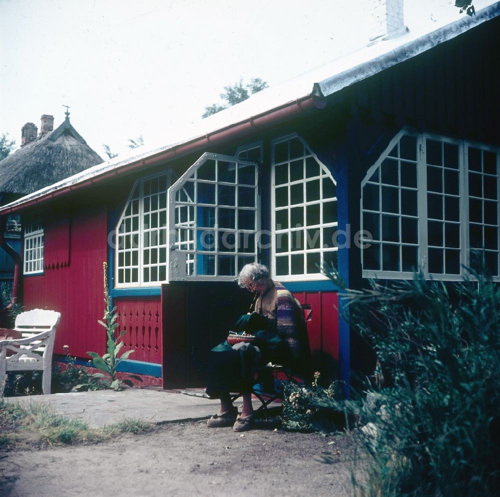 Ahrenshoop: Ein älterer Mann sitzt vor seinem roten Sommerhäuschen und näht in Ahrenshoop in Mecklenburg-Vorpommern in der DDR