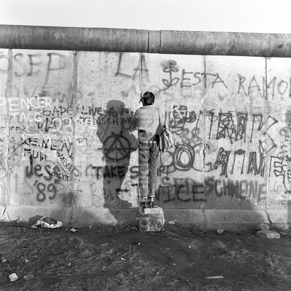 Berlin - Mitte: Ein Mann fotografiert durch einen Spalt in der Berliner Mauer in Berlin