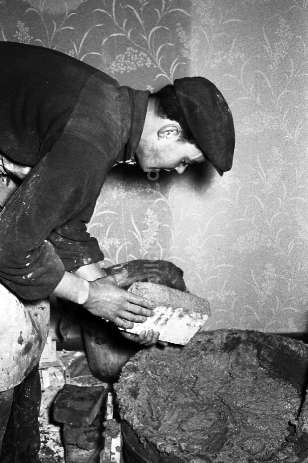 Zschopau: Ein Ofenbauer- Ofensetzer setzt einen Kachelofen in Zschopau in Sachsen in der DDR