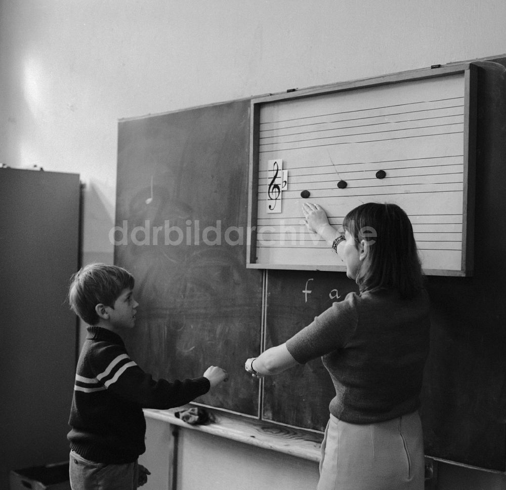 DDR-Bildarchiv: Berlin - Ein Schüler steht an der Tafel und die Musiklehrerin erklärt die Tonleiter in Berlin