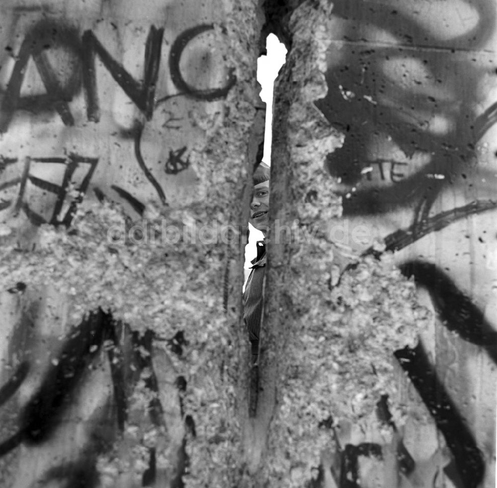 DDR-Bildarchiv: Berlin - Mitte - Ein Soldat der Grenztruppen der DDR schaut durch ein Loch in der Berliner Mauer in Berlin - Mitte