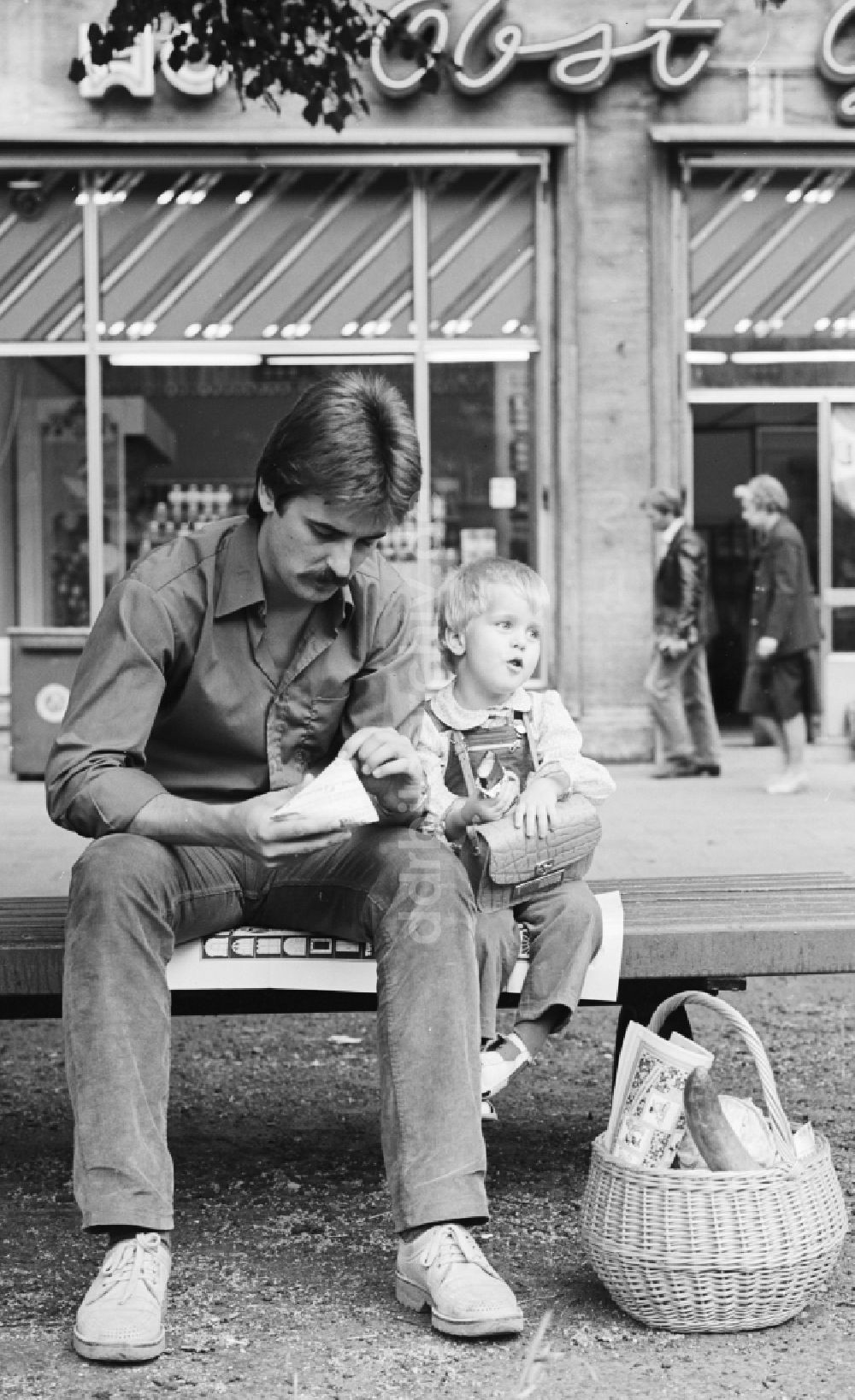 DDR-Bildarchiv: Berlin - Ein Vater sitzt mit seinem Kind auf einer Bank in der Karl-Marx-Allee in Berlin, der ehemaligen Hauptstadt der DDR, Deutsche Demokratische Republik