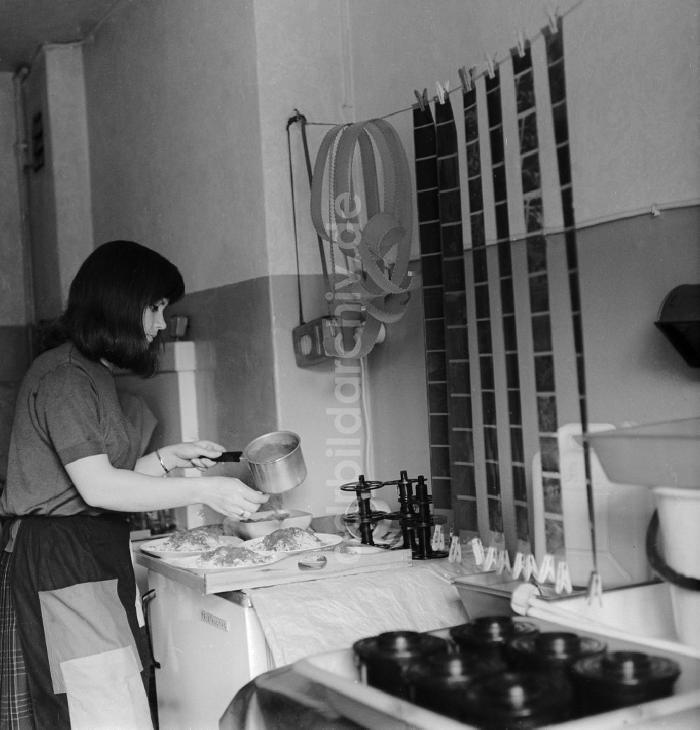 DDR-Fotoarchiv: Berlin - Eine Frau bereitet Essen zu, während in der Küche aufgehängte Filme trocknen in Berlin, der ehemaligen Hauptstadt der DDR, Deutsche Demokratische Republik