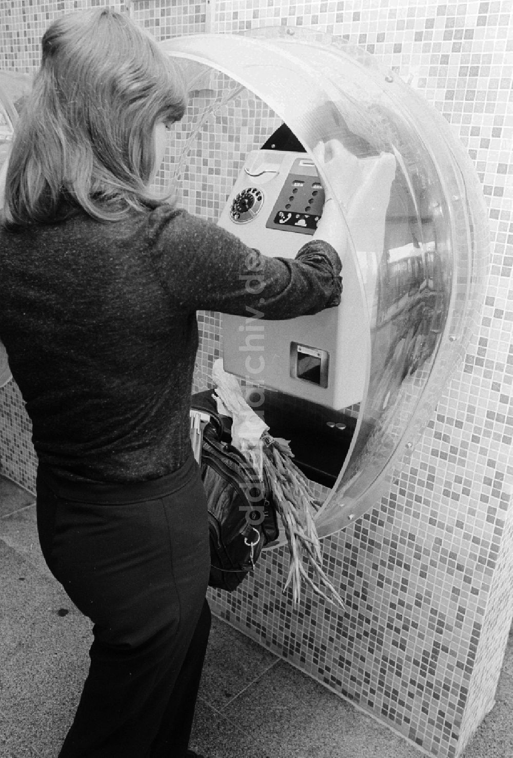 DDR-Fotoarchiv: Schönefeld - Eine Frau telefoniert mit einem Münzfernsprecher im Bahnhof Flughafen Berlin-Schönefeld in Schönefeld in Brandenburg in der DDR