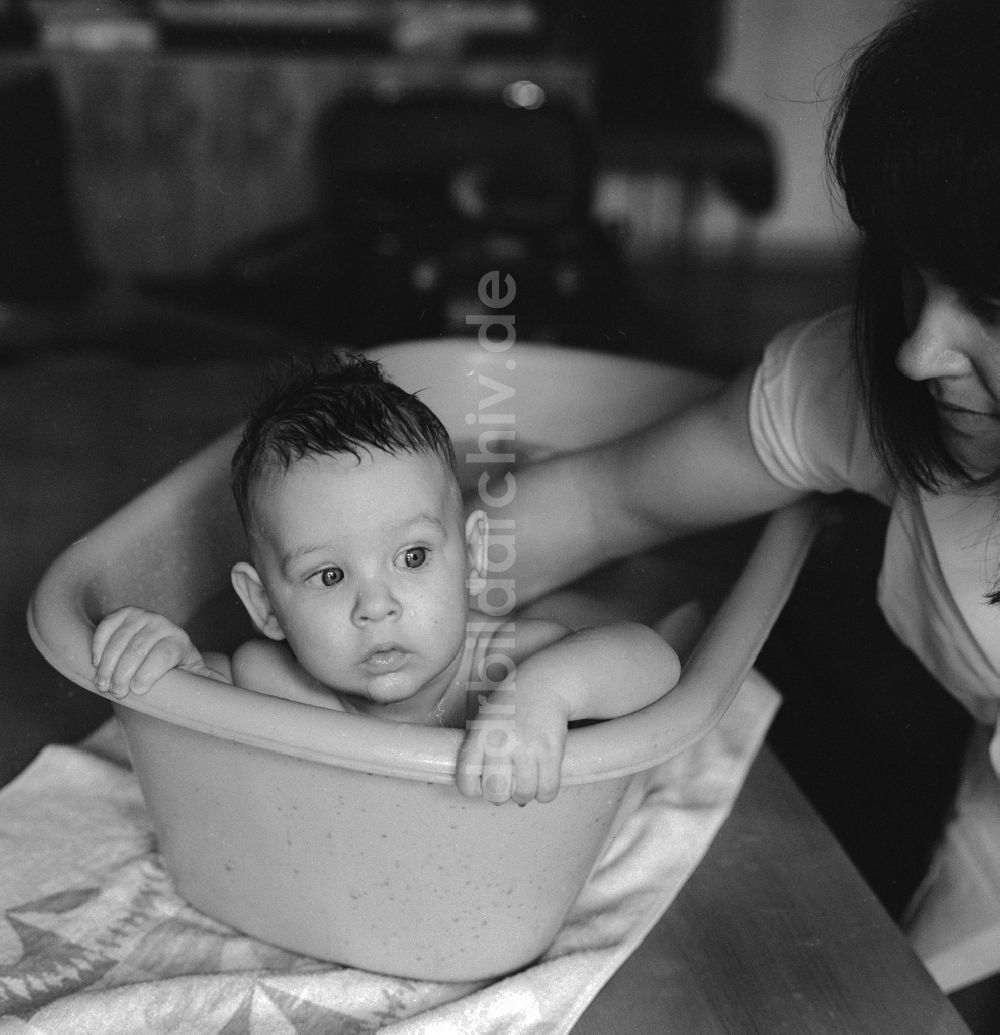 DDR-Fotoarchiv: Berlin - Eine Mutter badet ihr Baby in einer Plastik Badewanne in Berlin, der ehemaligen Hauptstadt der DDR, Deutsche Demokratische Republik