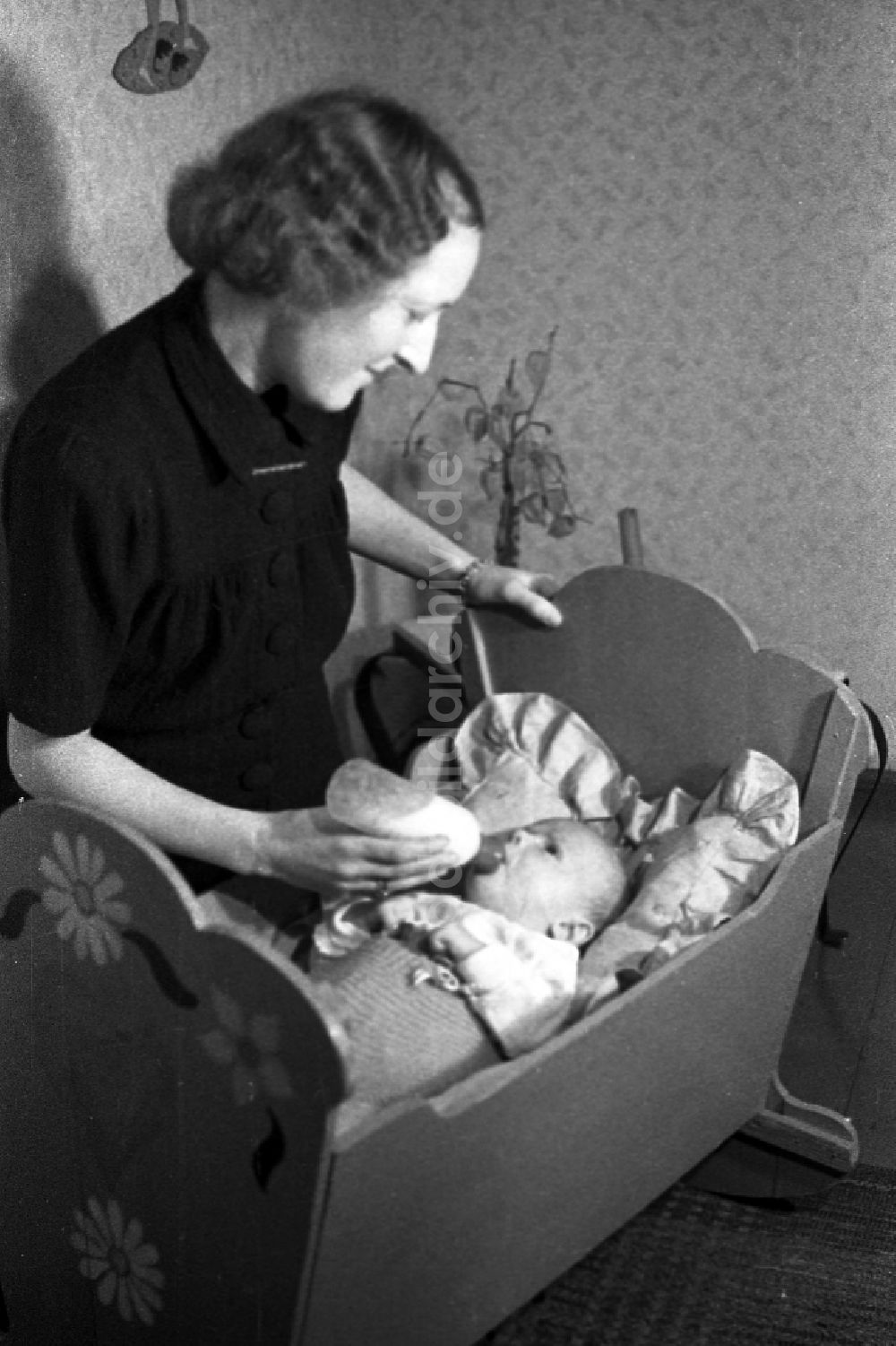 Merseburg: Eine Mutter gibt ihrem Baby in der Wiege die Nuckelflasche in Merseburg in Sachsen-Anhalt in der DDR