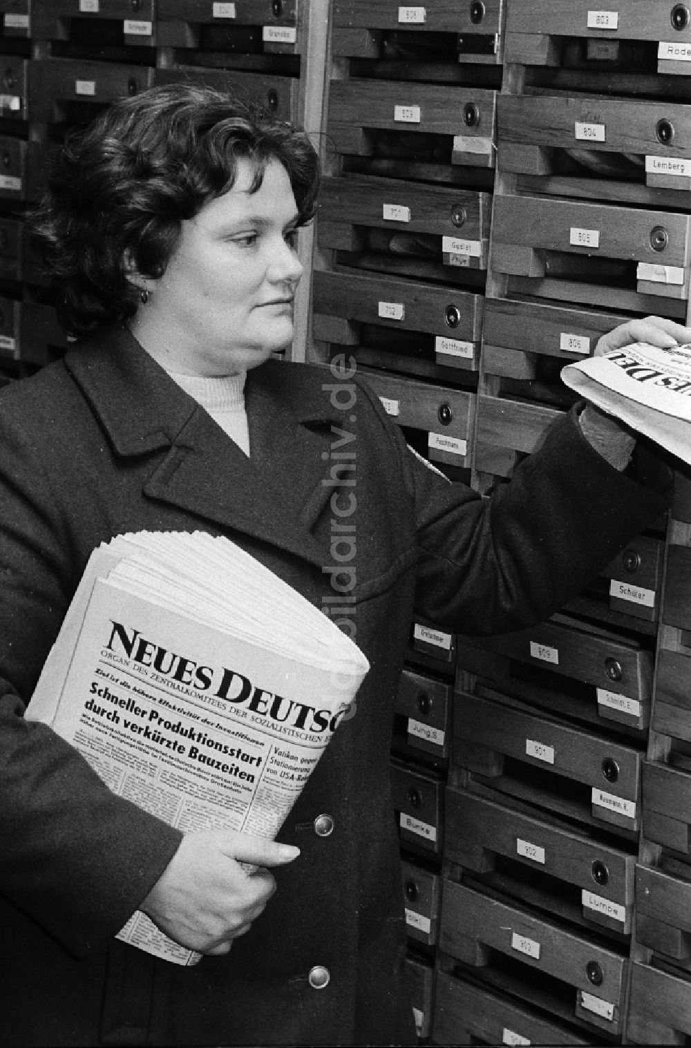 Berlin: Eine Postzustellerin steckt die tägliche sozialistische Tageszeitung Neues Deutschland in Briefkasten eines Mietshauses in Berlin, der ehemaligen Hauptstadt der DDR, Deutsche Demokratische Republik