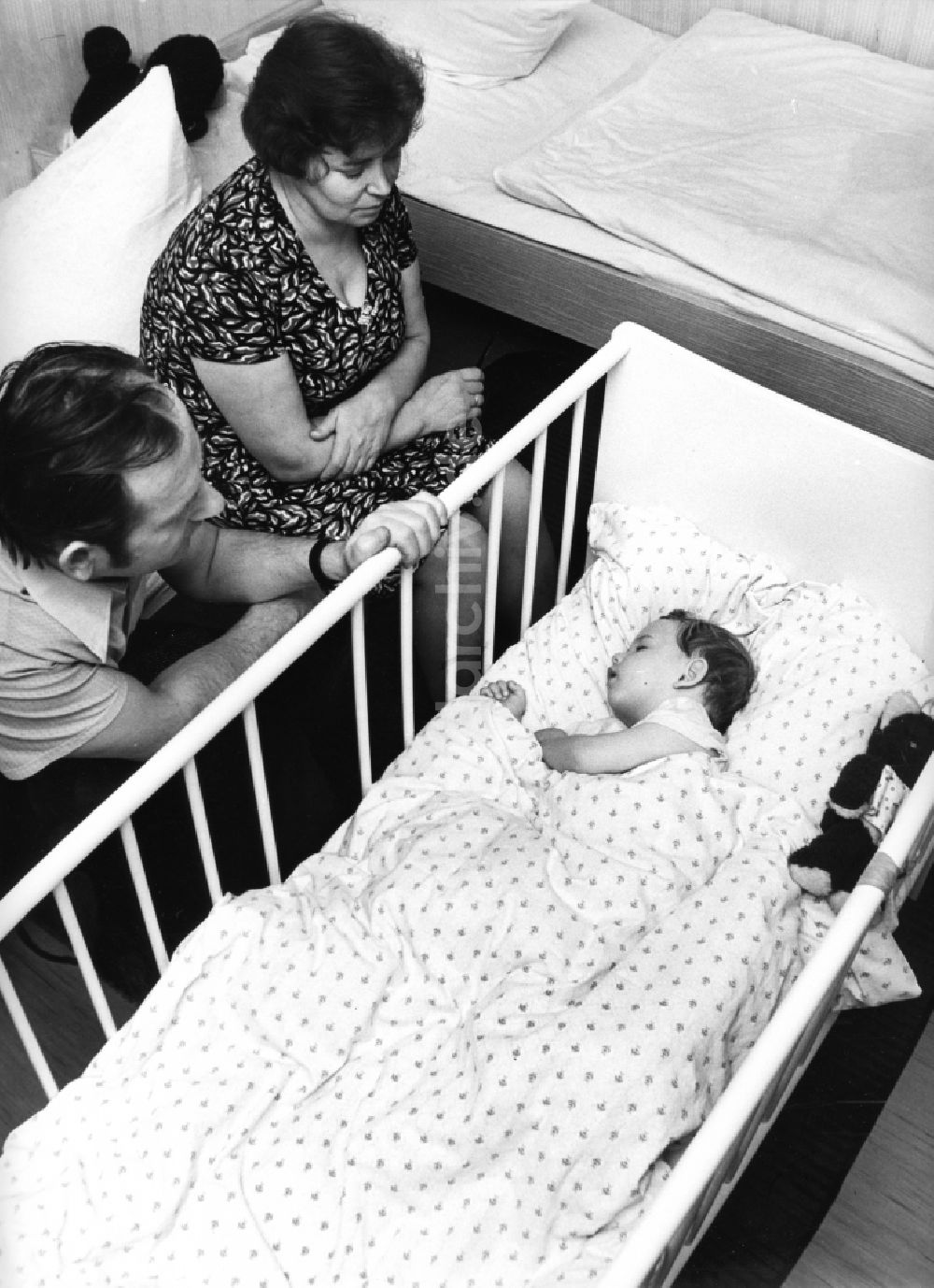 DDR-Bildarchiv: Boxberg/Oberlausitz - Eltern sitzen am Kinderbett ihres schlafenden Kindes in Boxberg/Oberlausitz in Sachsen in der DDR