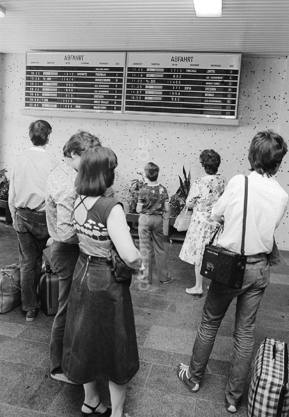 DDR-Bildarchiv: Schönefeld - Fahrgäste informieren sich an der Anzeigetafel über Abfahrt und Ankunft der Züge im Bahnhof Flughafen Berlin-Schönefeld in Schönefeld in Brandenburg in der DDR