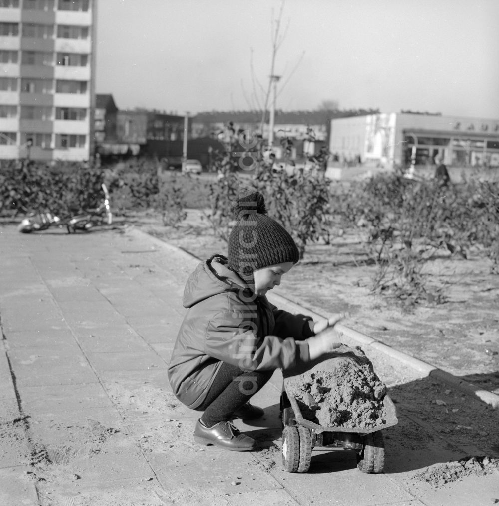 DDR-Fotoarchiv: Berlin - Junge mit Pudelmütze spielt mit seinem Plastik LKW im Sandkasten in einem Innenhof eines Wohngebietes in Berlin, der ehemaligen Hauptstadt der DDR, Deutsche Demokratische Republik