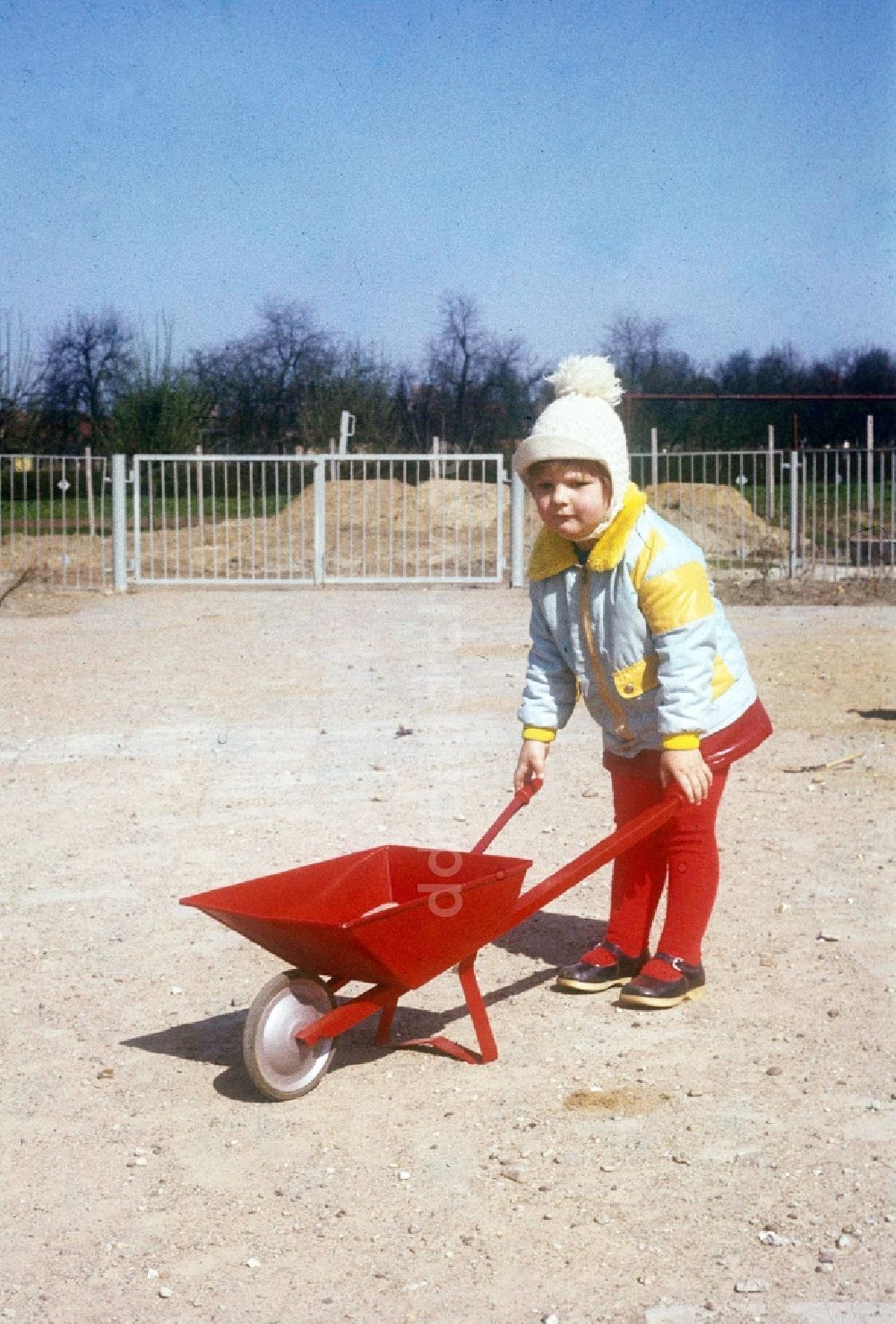Neustrelitz: Kind mit einer roten Schubkarre und Pudelmütze in Neustrelitz in Mecklenburg-Vorpommern in der DDR