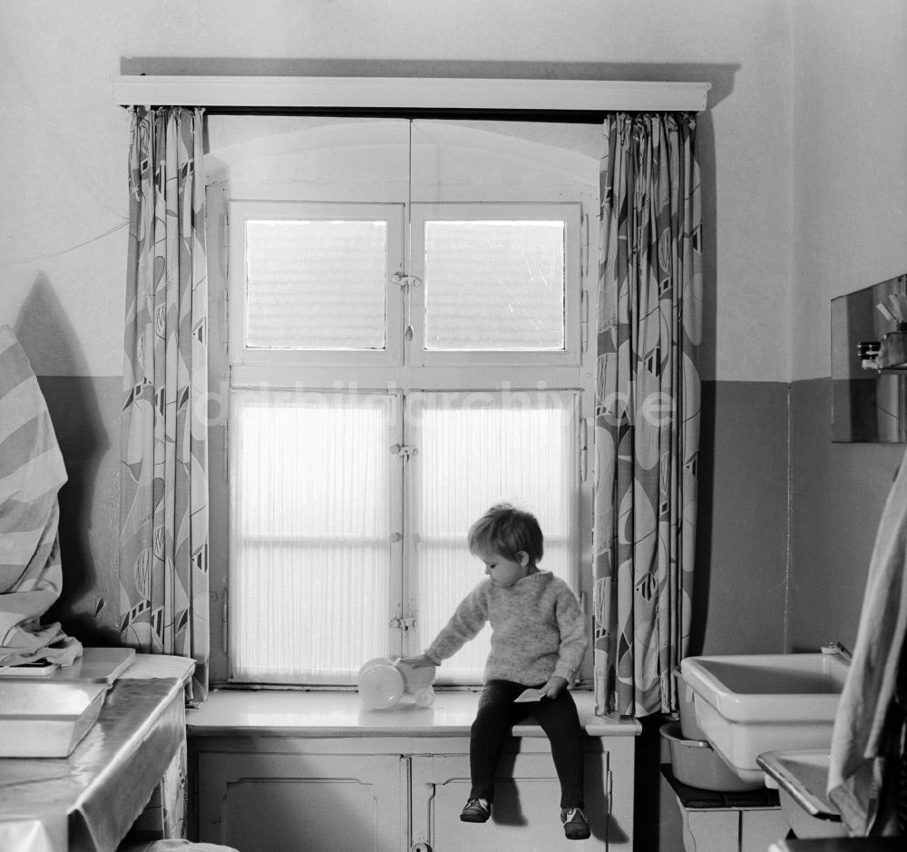 DDR-Fotoarchiv: Berlin - Kind sitzt auf einem Fensterbrett mit seinem Spielzeug in Berlin, der ehemaligen Hauptstadt der DDR, Deutsche Demokratische Republik