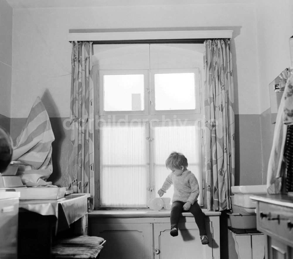 Berlin: Kind sitzt auf einem Fensterbrett mit seinem Spielzeug in Berlin, der ehemaligen Hauptstadt der DDR, Deutsche Demokratische Republik