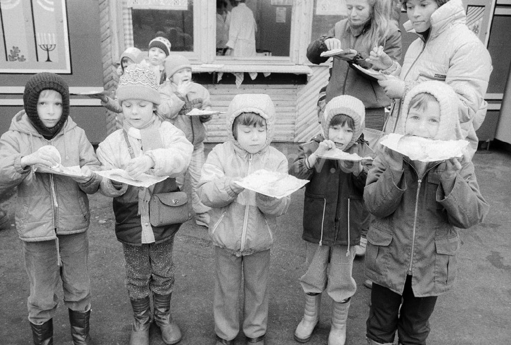 DDR-Fotoarchiv: Berlin - Kinder essen gefüllte Eierkuchen auf dem Weihnachtsmarkt in Berlin, der ehemaligen Hauptstadt der DDR, Deutsche Demokratische Republik