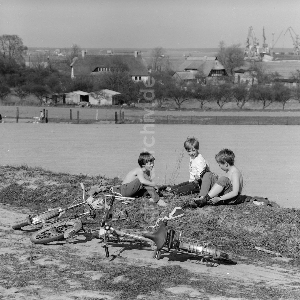 Rostock: Kinder die ihre Fahrräder abgelegt haben sitzen am Feldrand in Rostock in Mecklenburg-Vorpommern in der DDR