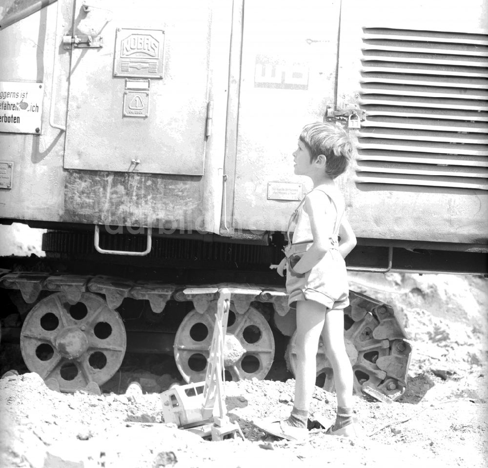 DDR-Bildarchiv: Berlin - Kleiner Junge in Lederhosen spielt mit seinem Holzbagger auf einer Baustelle neben einem Großbagger in Berlin, der ehemaligen Hauptstadt der DDR, Deutsche Demokratische Republik
