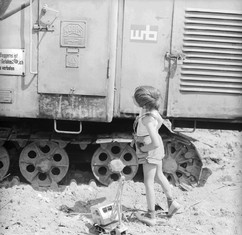Berlin: Kleiner Junge in Lederhosen spielt mit seinem Holzbagger auf einer Baustelle neben einem Großbagger in Berlin, der ehemaligen Hauptstadt der DDR, Deutsche Demokratische Republik