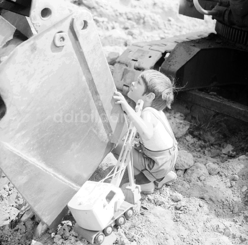 DDR-Bildarchiv: Berlin - Kleiner Junge in Lederhosen spielt mit seinem Holzbagger auf einer Baustelle neben einem Großbagger in Berlin, der ehemaligen Hauptstadt der DDR, Deutsche Demokratische Republik