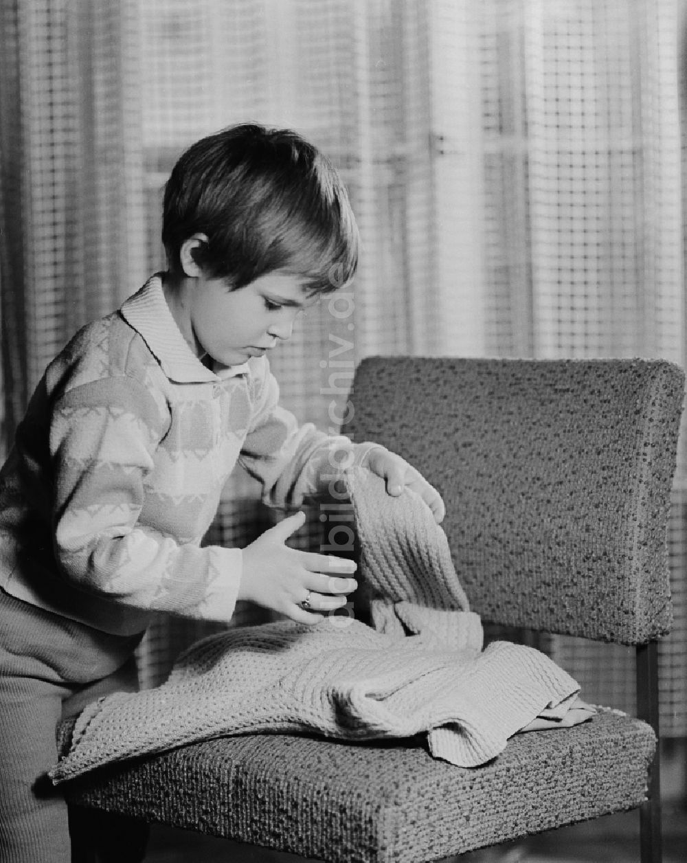 DDR-Fotoarchiv: Berlin - Kleines Kind beim zusammenlegen eines Pullovers in Berlin