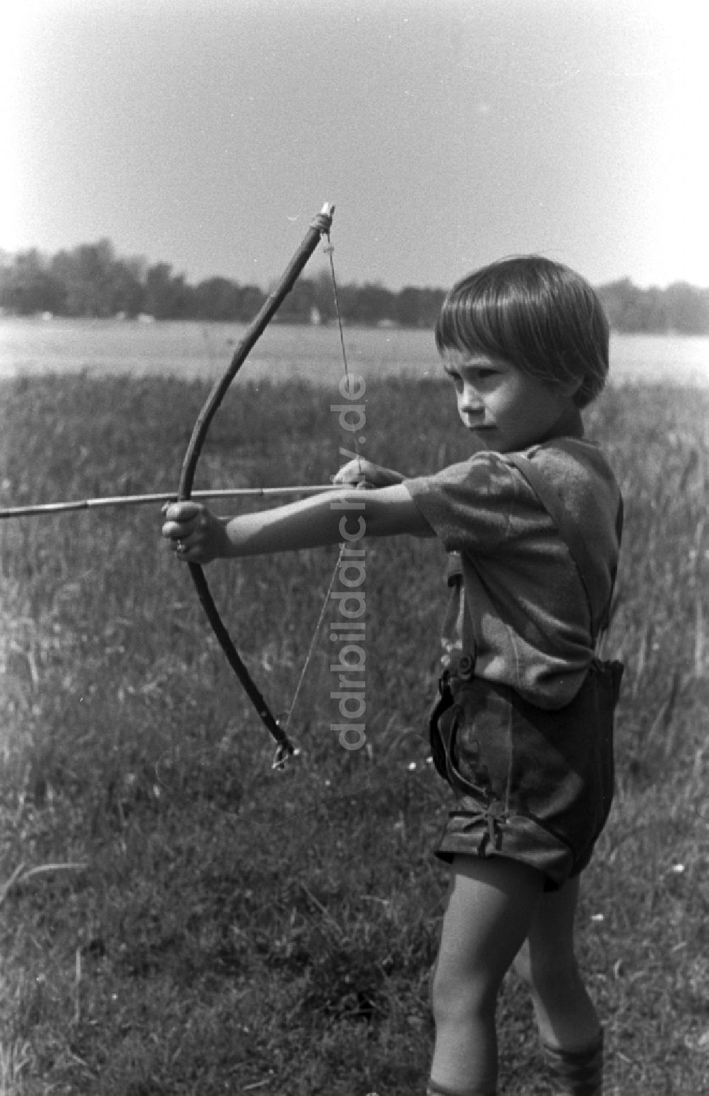 DDR-Bildarchiv: Kirchmöser - Kleines Kind in Lederhosen mit Pfeil und Bogen auf einer Wiese in Brandenburg