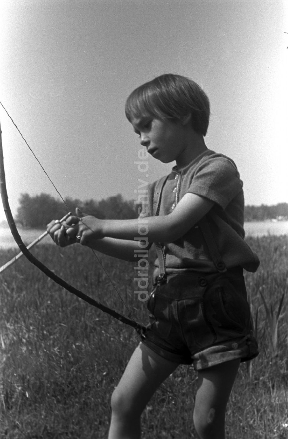 DDR-Fotoarchiv: Kirchmöser - Kleines Kind in Lederhosen mit Pfeil und Bogen auf einer Wiese in Brandenburg