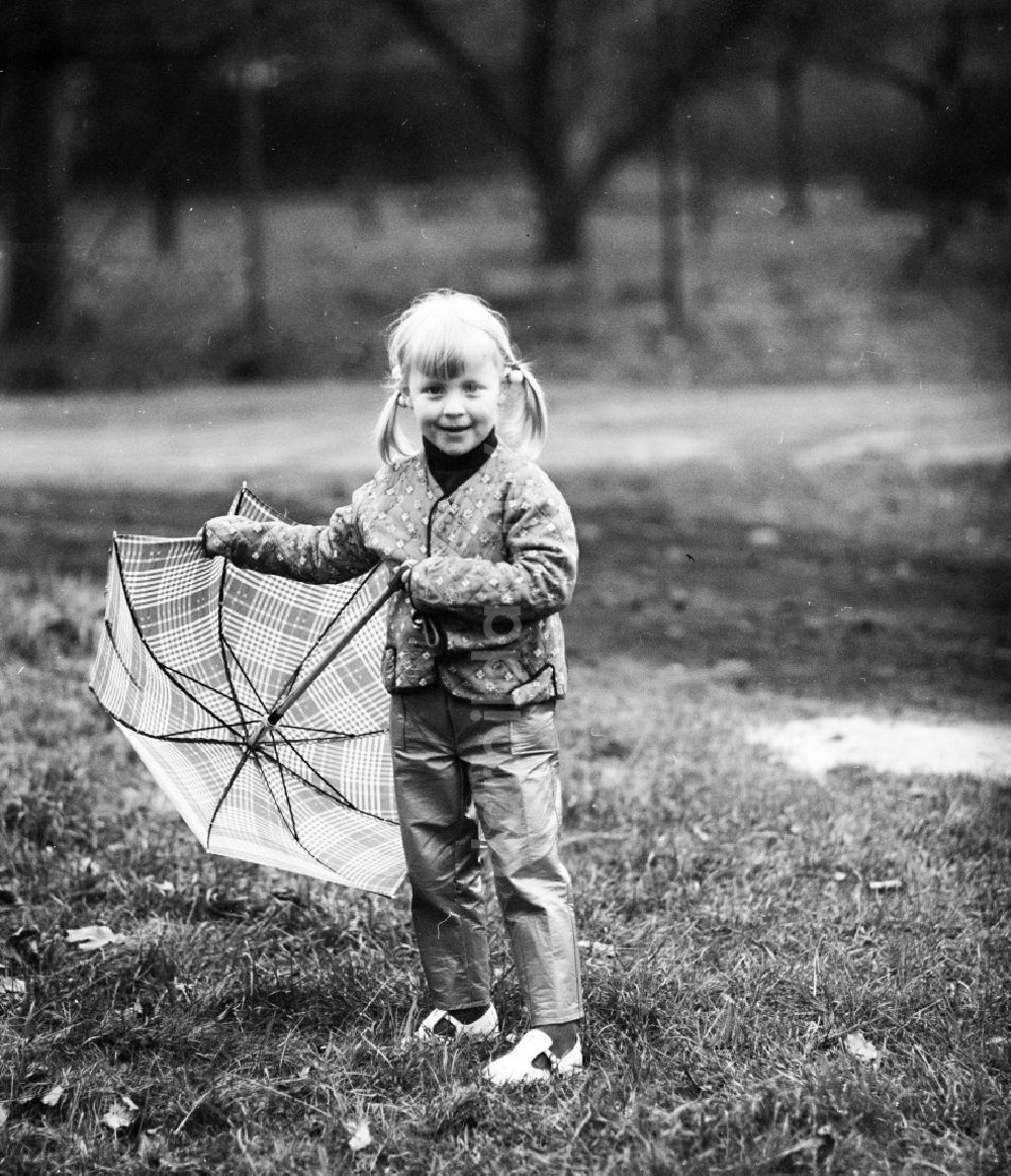 DDR-Bildarchiv: Berlin - Kleines Mädchen mit Zöpfen steht mit einem Regenschirm auf einer Wiese in Berlin, der ehemaligen Hauptstadt der DDR, Deutsche Demokratische Republik