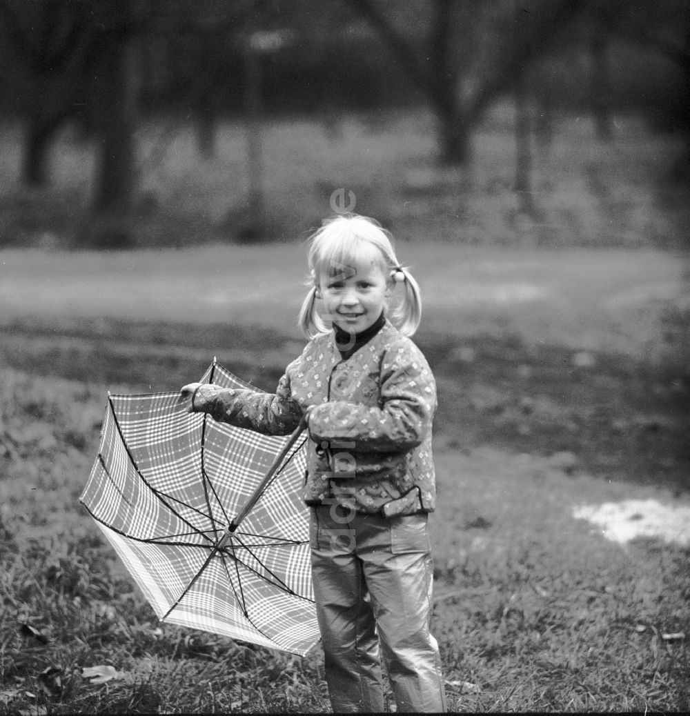 DDR-Fotoarchiv: Berlin - Kleines Mädchen mit Zöpfen steht mit einem Regenschirm auf einer Wiese in Berlin, der ehemaligen Hauptstadt der DDR, Deutsche Demokratische Republik