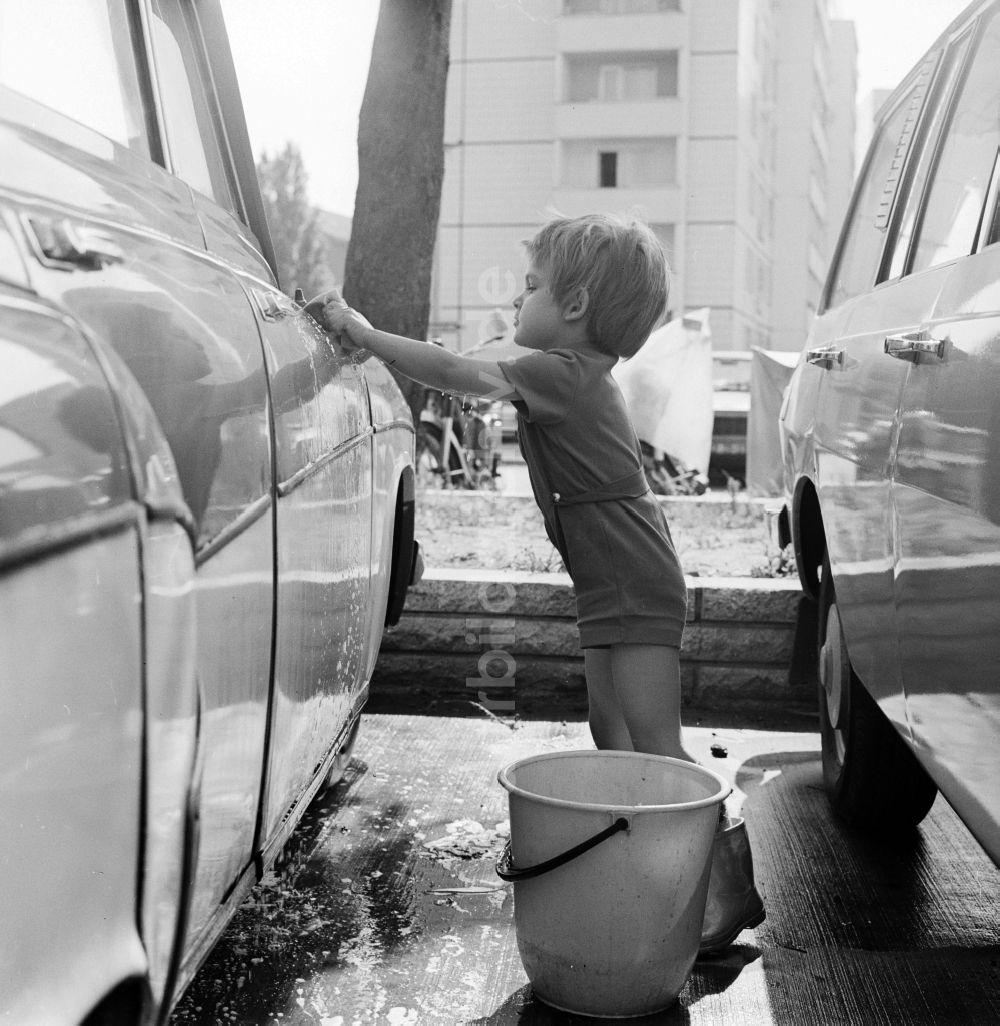 DDR-Fotoarchiv: Berlin - Kleinkind beim Auto waschen auf einem Parkplatz in Berlin, der ehemaligen Hauptstadt der DDR, Deutsche Demokratische Republik