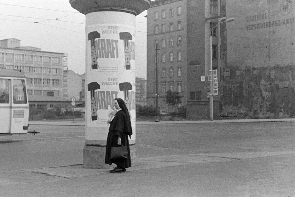 DDR-Bildarchiv: Leipzig - Litfaßsäule mit Werbung Seht welche Kraft mit vorbeilaufender Nonne in Leipzig in der DDR