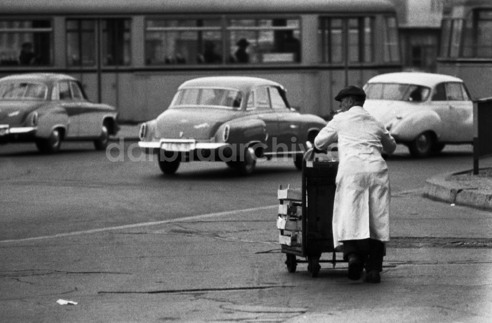 Berlin: Mann schiebt einen Transportwagen mit leeren Holzkisten über die Straße in Berlin in der DDR