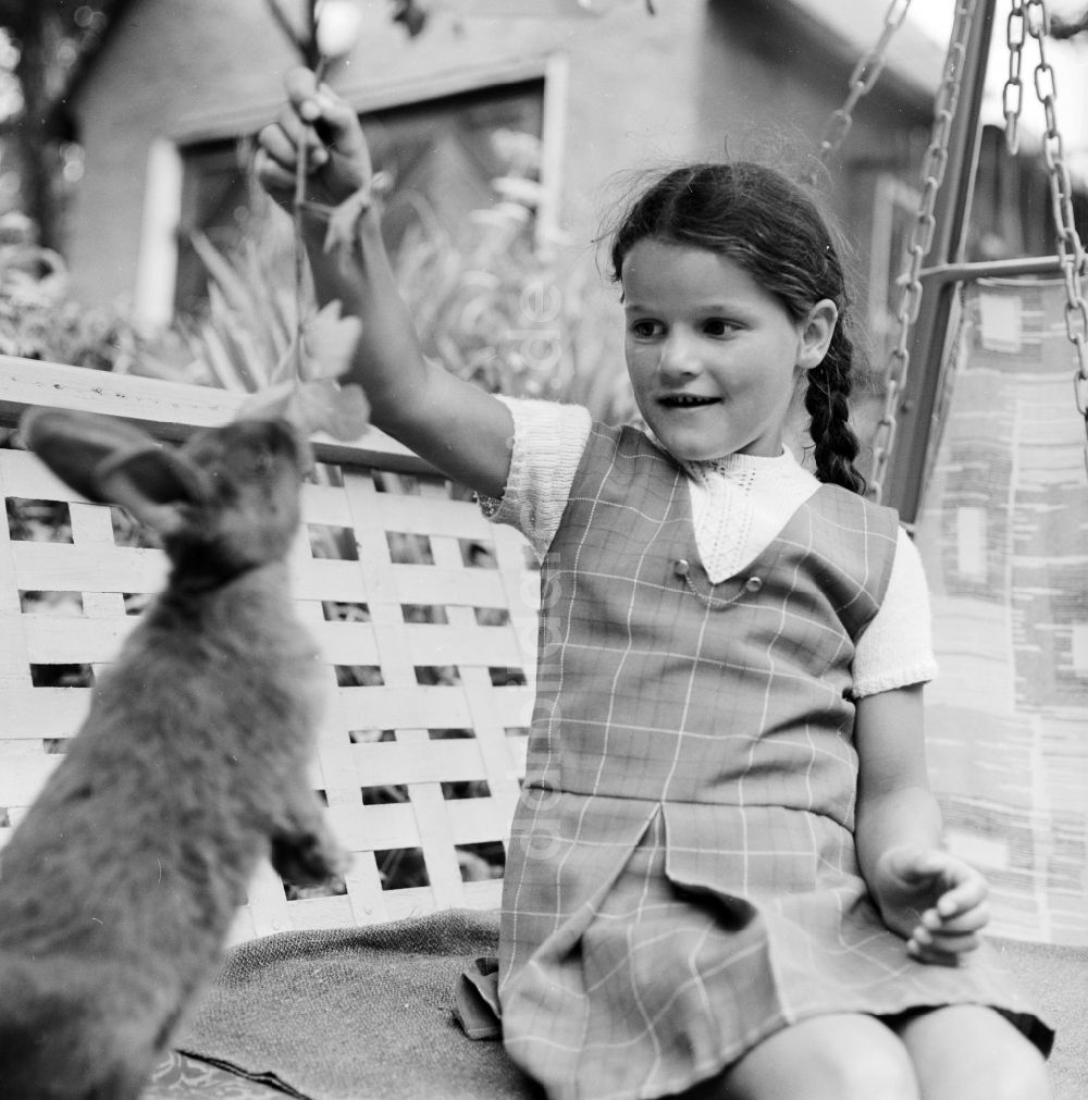 Scheibenberg: Mädchen sitzt mit einem Kaninchen auf einer Gartenschaukel in Scheibenberg in Sachsen in der DDR