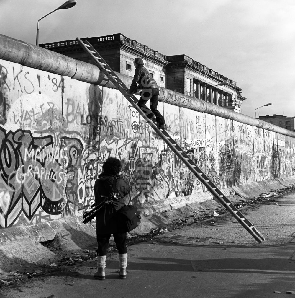 Berlin - Mitte: Neugierig klettern Schaulustige auf einer Leiter an der Berliner Mauer empor