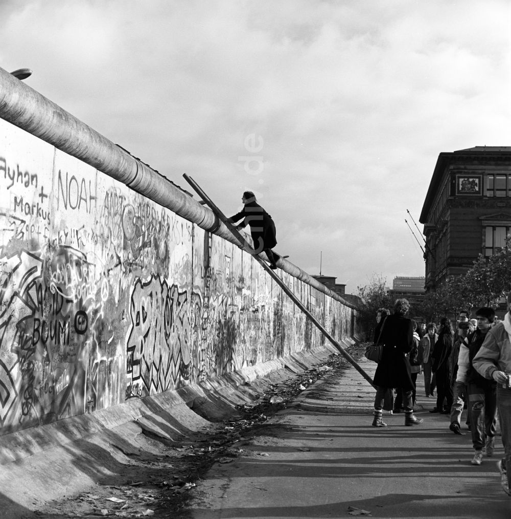 Berlin - Mitte: Neugierig klettern Schaulustige auf einer Leiter an der Berliner Mauer empor
