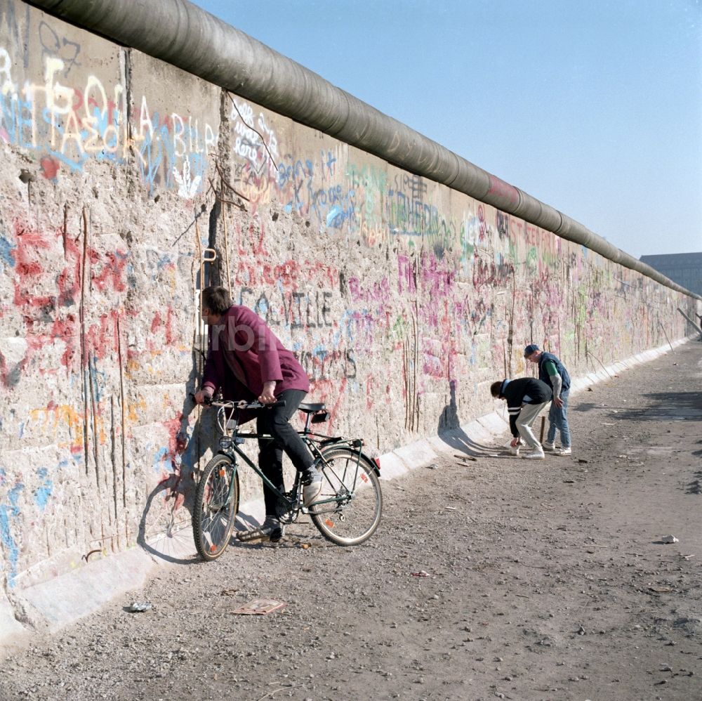DDR-Bildarchiv: Berlin - Neugierig schaut ein Radfahrer durch ein Loch in der Berliner Mauer in Berlin