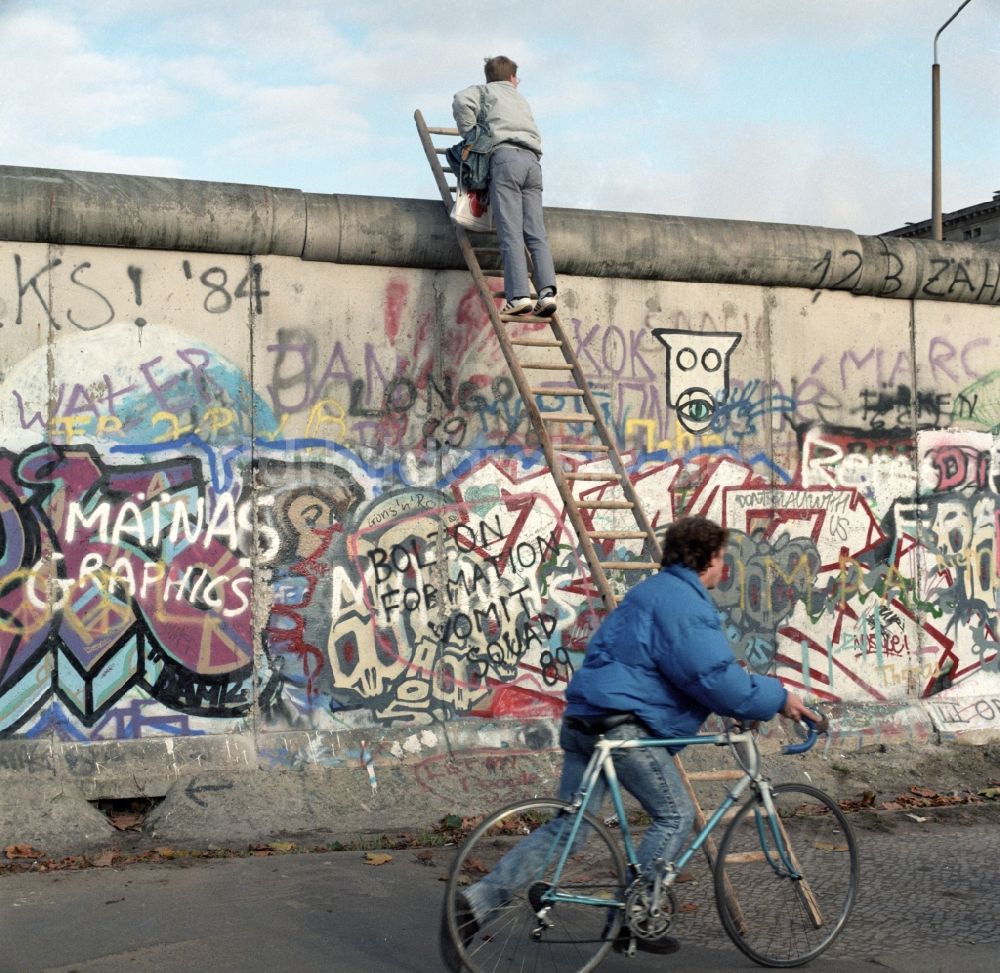 Berlin - Mitte: Neugieriger Mann klettert mit Hilfe einer Leiter an der Berliner Mauer hoch
