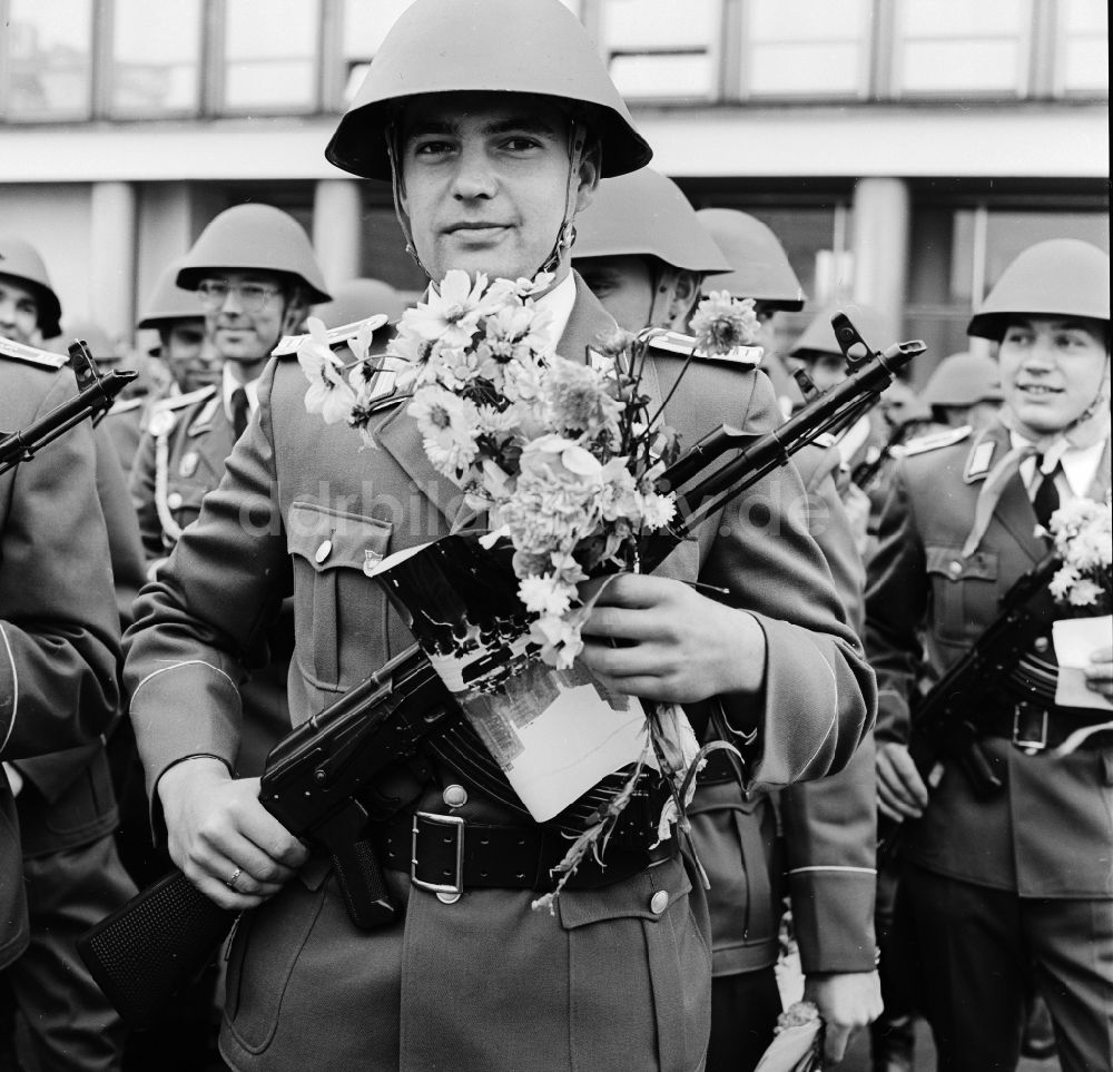 Berlin: Soldat der NVA mit Stahlhelm, einem Sturmgewehr vom Typ AK-47 und Blumen in der Hand in Berlin, der ehemaligen Hauptstadt der DDR, Deutsche Demokratische Republik