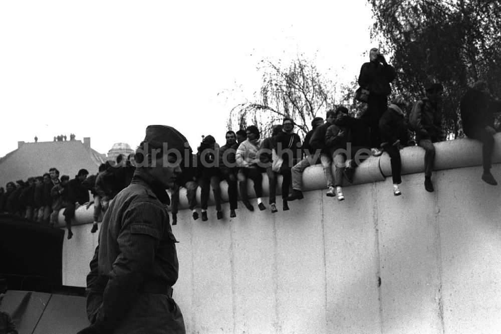 DDR-Bildarchiv: Berlin - Soldaten der DDR stehen in einer Reihe vor der Berliner-Mauer am Potzdamer Platz, auf der Mauer sitzen und stehen Menschen