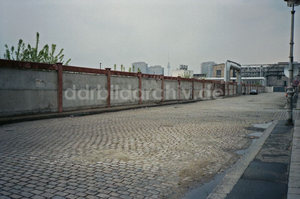 Berlin: Straßenzustand einer Kopfsteinpflasterstraße an einer Industriegebiets- Mauer im Ortsteil Friedrichshain in Berlin in der DDR