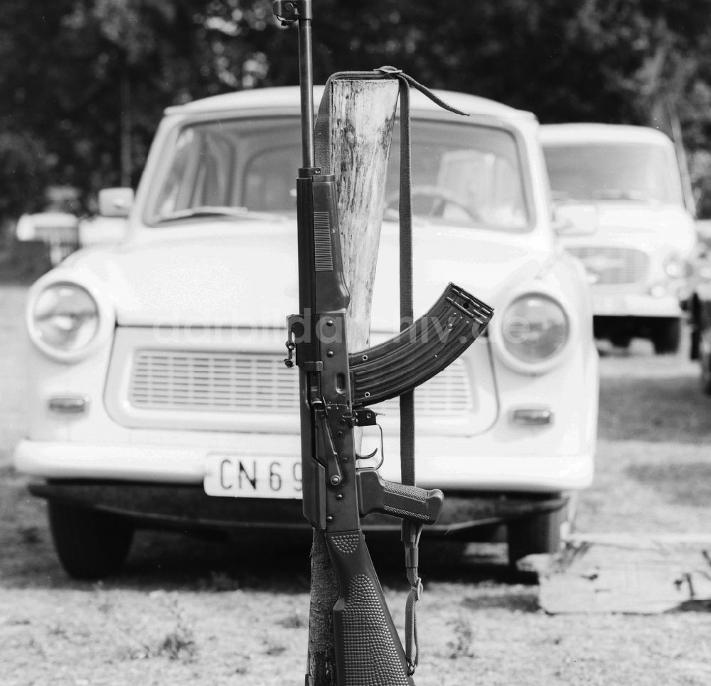 DDR-Fotoarchiv: Ferdinandshof - Symbolbild, ein Gewehr der Marke AK 47 vor einem Trabant in Ferdinandshof in Mecklenburg-Vorpommern in der DDR