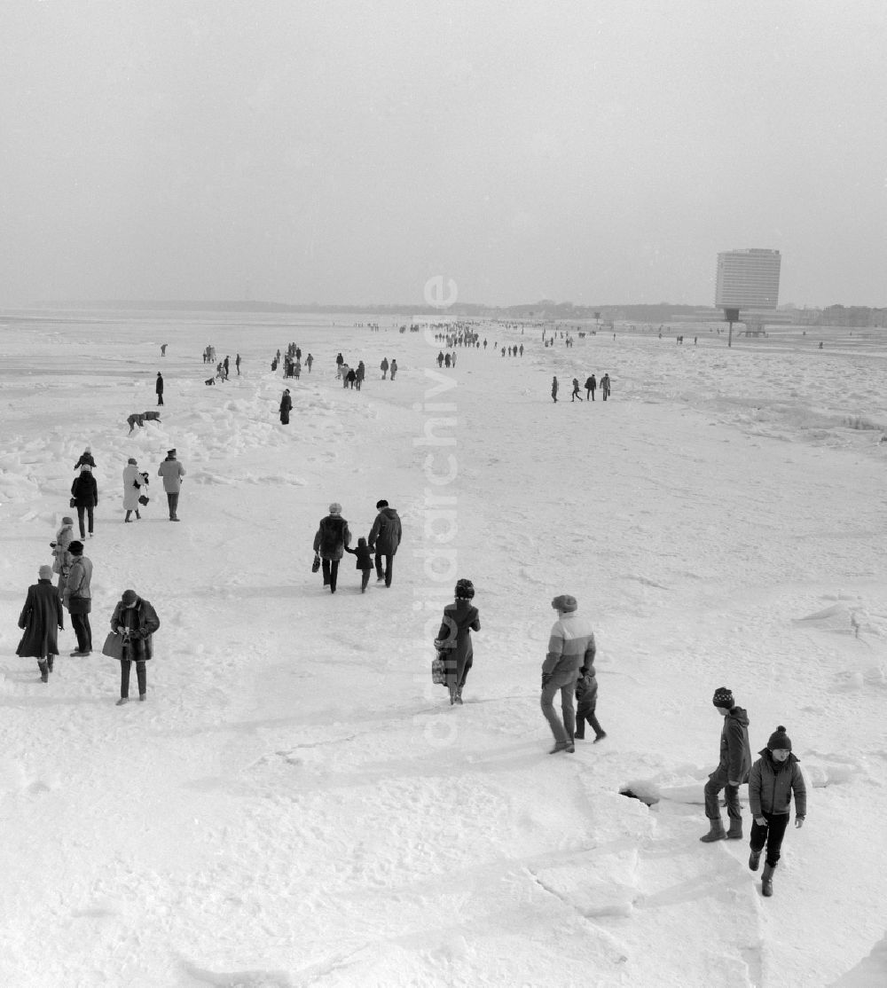 Warnemünde: Touristen spazieren auf der zugefrorenen und schneebedeckten Ostsee in Warnemünde in Mecklenburg Vorpommern in der DDR