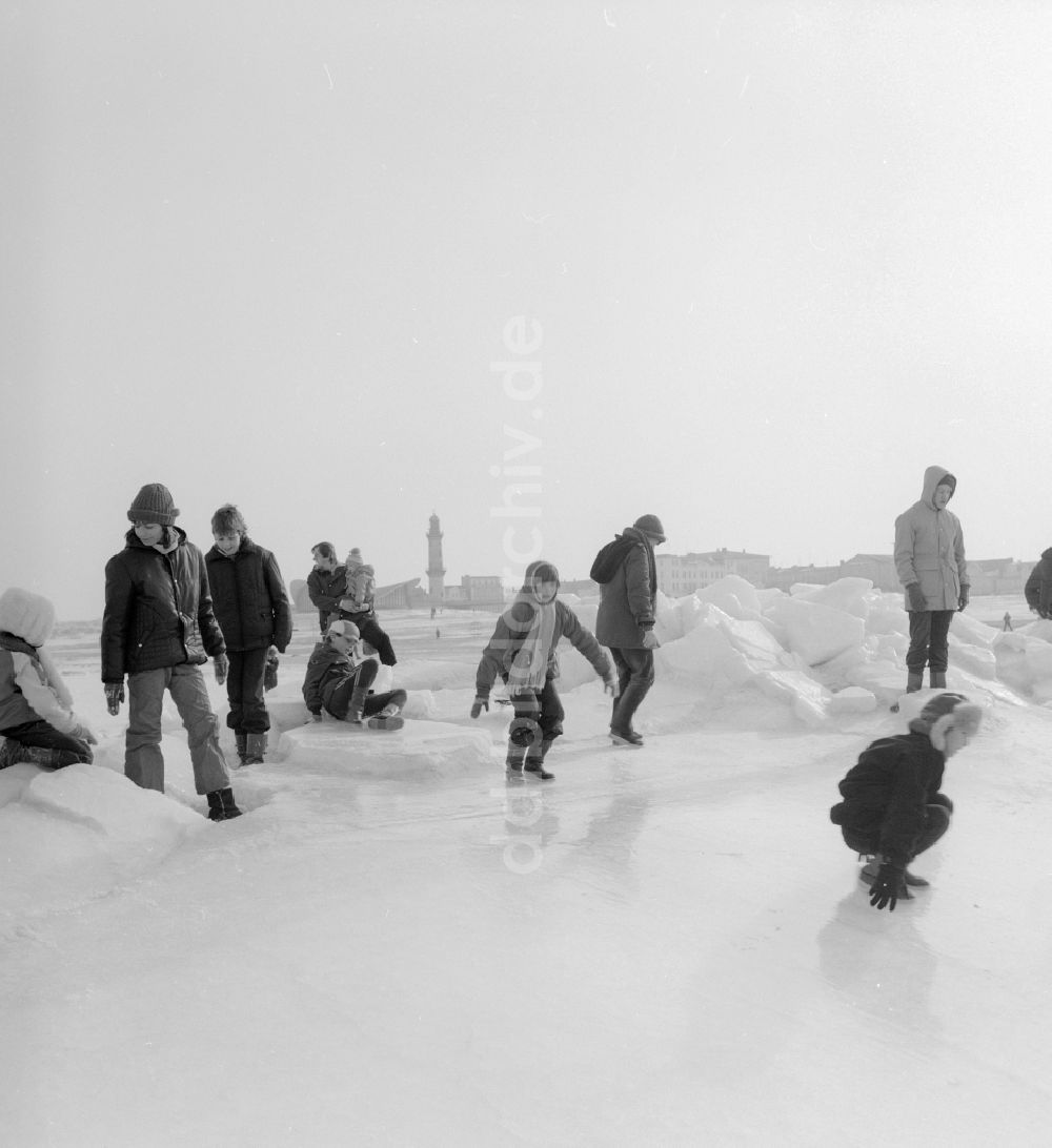 Warnemünde: Touristen spazieren auf der zugefrorenen und schneebedeckten Ostsee in Warnemünde in Mecklenburg Vorpommern in der DDR
