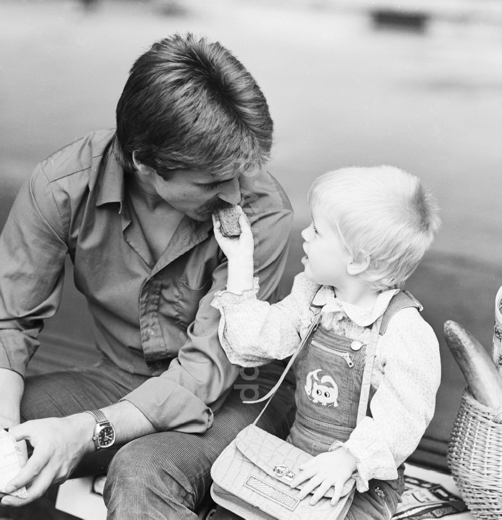 DDR-Fotoarchiv: Berlin - Vater sitzt mit seinem Kind auf einer Bank in Berlin, der ehemaligen Hauptstadt der DDR, Deutsche Demokratische Republik