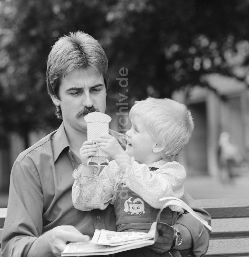 DDR-Fotoarchiv: Berlin - Vater sitzt mit seinem Kind auf einer Bank in Berlin, der ehemaligen Hauptstadt der DDR, Deutsche Demokratische Republik