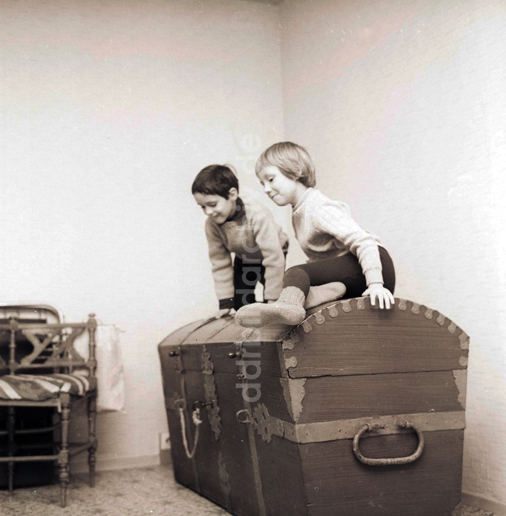 DDR-Fotoarchiv: Berlin - Zwei Kinder sitzen auf einer großen alten Holztruhe in Berlin, der ehemaligen Hauptstadt der DDR, Deutsche Demokratische Republik