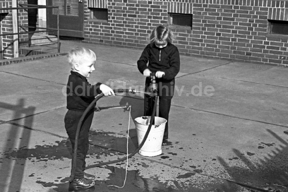 DDR-Fotoarchiv: Merseburg - Zwei Kinder spielen im Innenhof mit einem Wasserschlauch in Merseburg in Sachsen-Anhalt in Deutschland